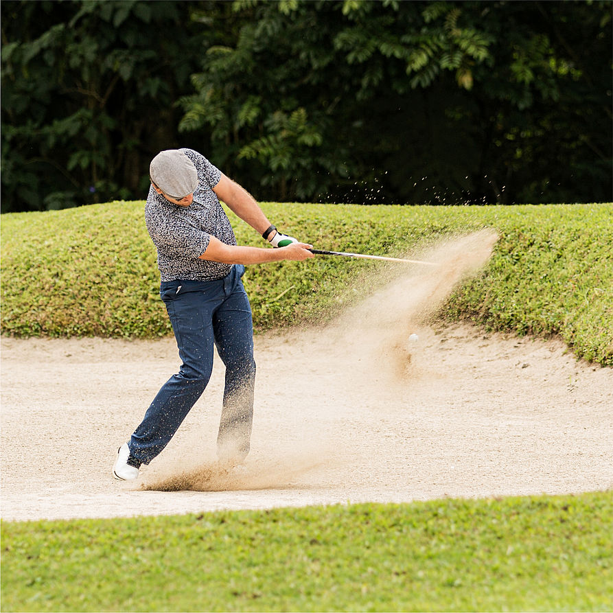 Mann schlägt Golfball aus dem Sand