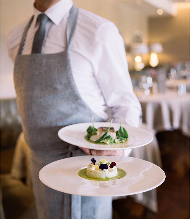 Waiter brings two plates with one arm at Genuss Hotel Schenna