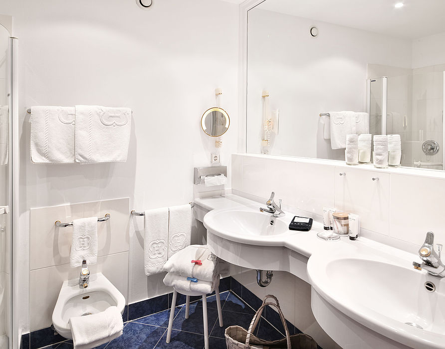 White bathroom with blue floor tiles, two washbasins, bidet and shower