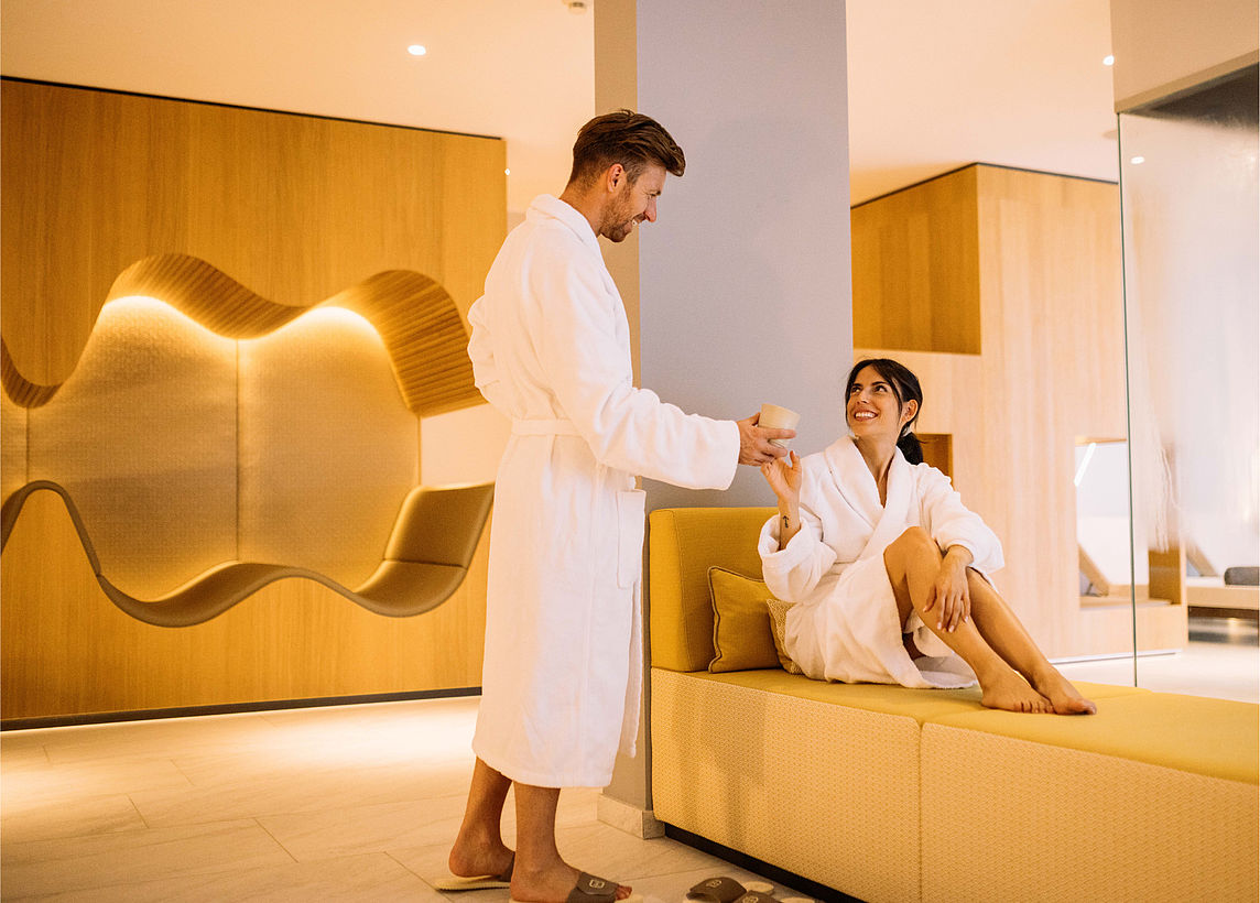 Mann gibt Frau etwas zum Trinken in Sauna im Wellness Hotel Schenna