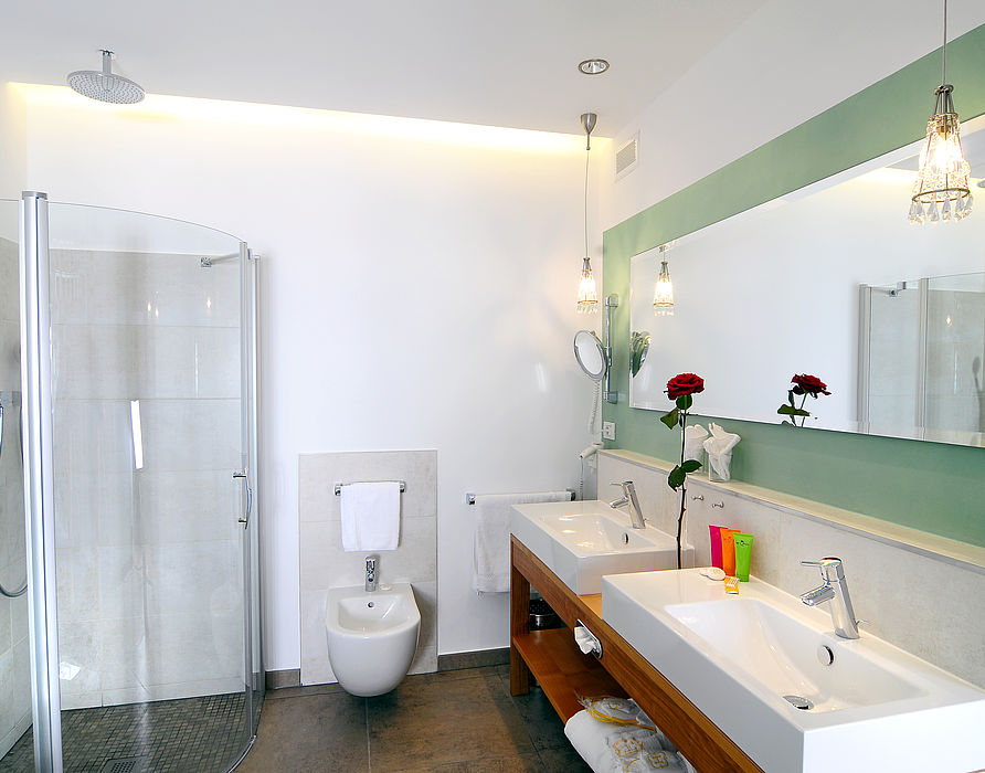 Badezimmer mit Dusche, Bidet, zwei Waschbecken und Spiegel mit grüner Wand