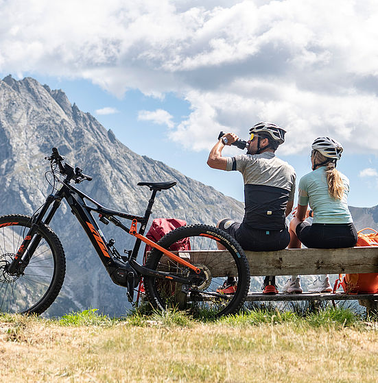 Coppia seduta su panchina in un paesaggio montano con ruote parcheggiate